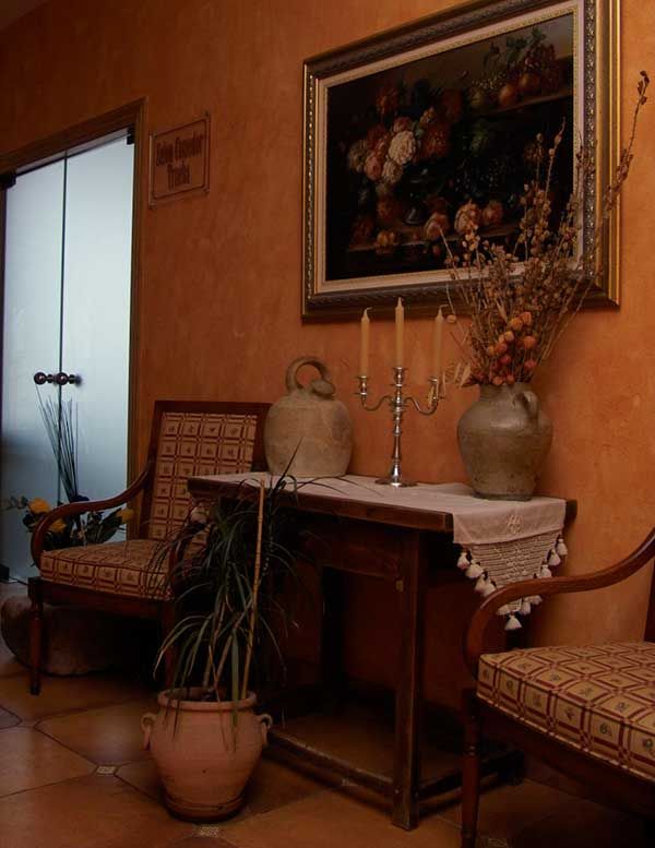 Entrada decorada con bodegón de flores, mesa con candelabro y butacas